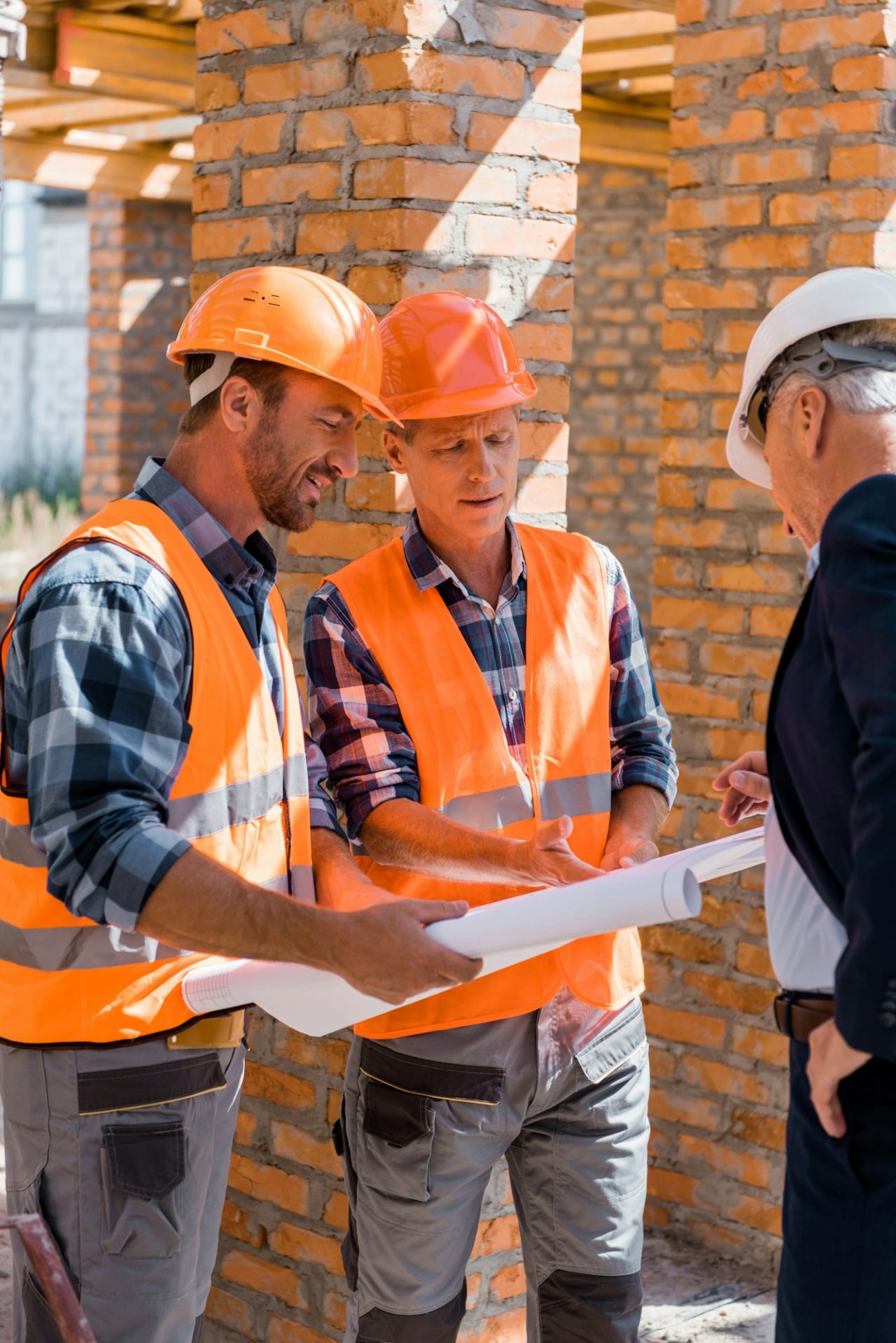 selective focus of constructors near mature businessman in suit looking at blueprint